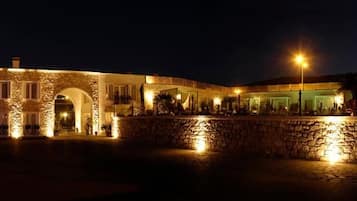 A stone building with an arched entrance, illuminated by exterior lights, and a stone wall in the foreground.