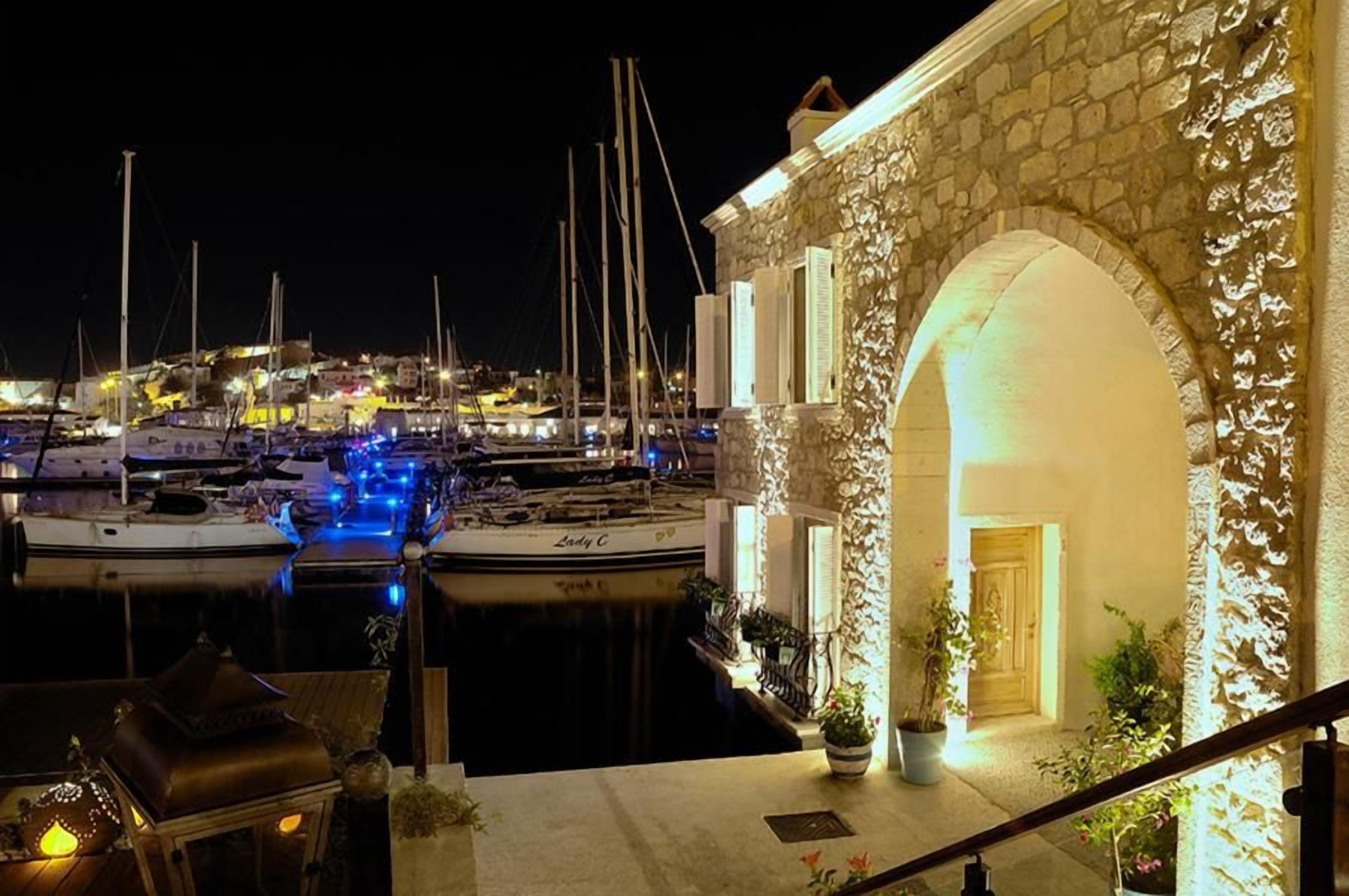 Una marina de noche con barcos amarrados, un edificio de piedra con un arco y una escalera que conduce a la entrada.