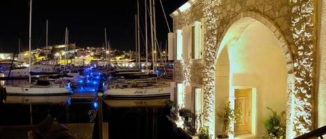 A marina at night with boats docked, a stone building with an archway, and a staircase leading to the entrance.