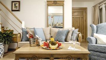 Een woonkamer met een houten salontafel, een bank met decoratieve kussens, een grote spiegel en uitzicht op een haven door het raam.