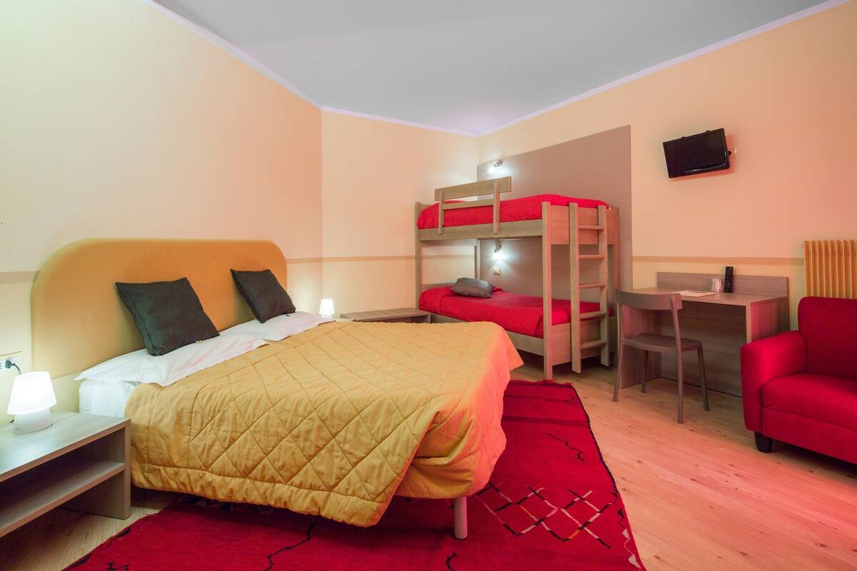 A hotel room with a bunk bed, a desk, a chair, and a TV.