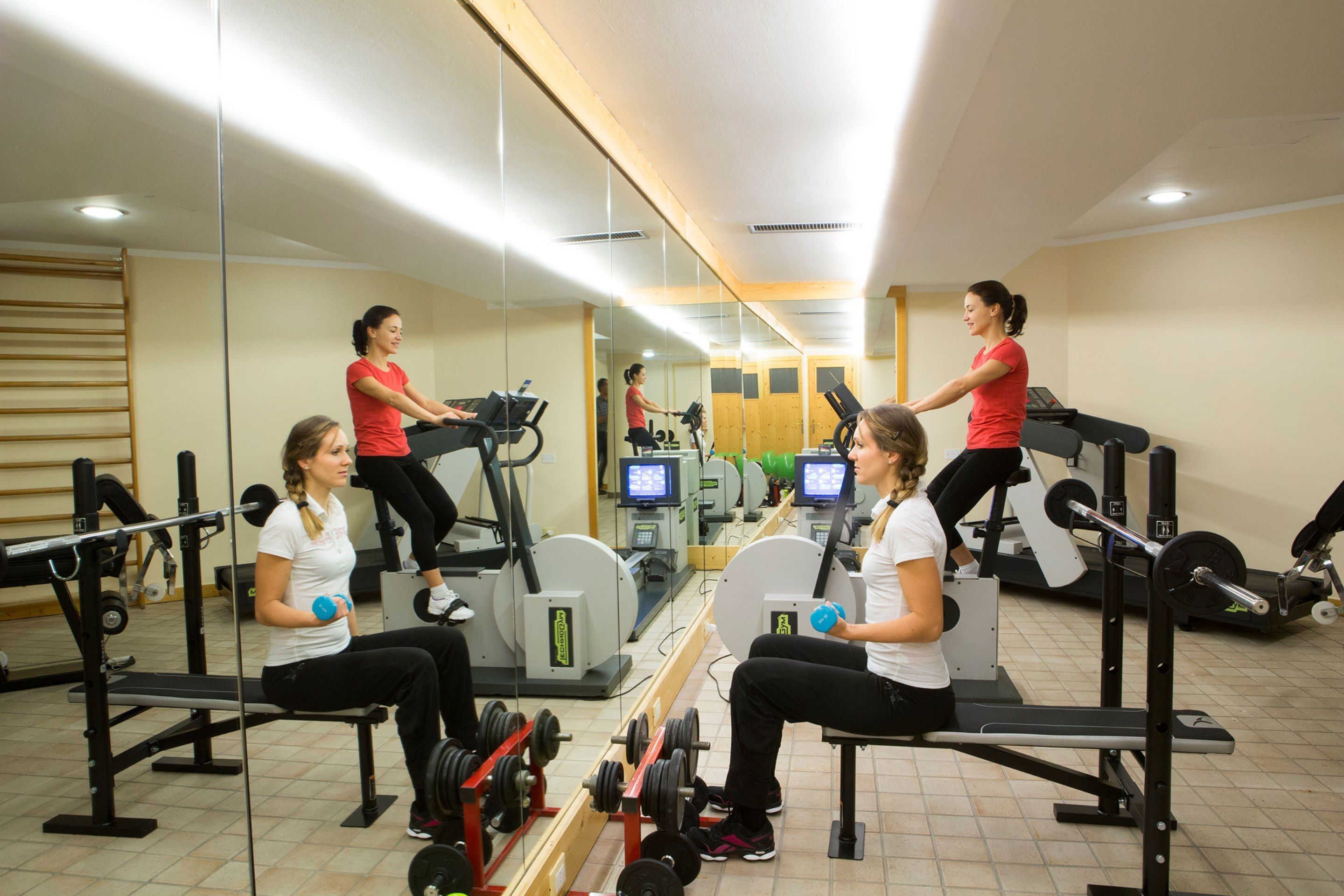 Een sportschool met trainingsapparatuur, spiegels en een loopband.