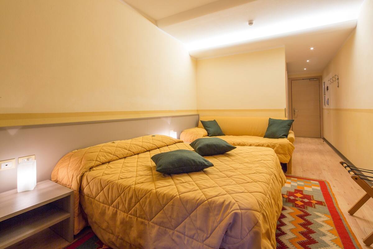 A hotel room with two beds, a nightstand, a small table, and a patterned rug.