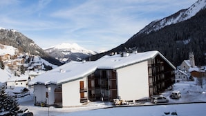 Un village de montagne enneigé, avec un bâtiment remarquable doté de grandes fenêtres et d’un toit en pente.
