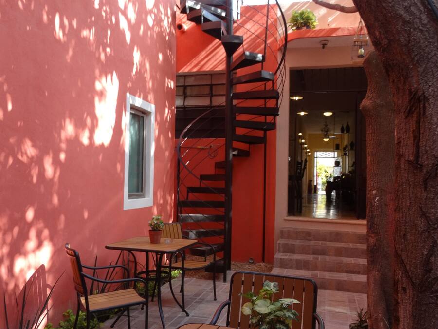 A patio with a wooden table and chairs, a spiral staircase, and a red building facade.