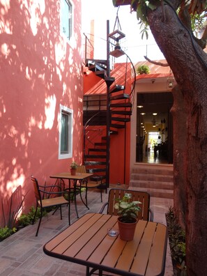 A patio with a wooden table and chairs, a spiral staircase, and a red building facade. - Casa San Juan (Mérida)