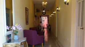 A hallway with a patterned floor, a purple armchair, a small table with a vase, and wall sconces. - Casa San Juan (Mérida)