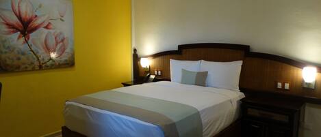 Habitación de hotel con cama, mesitas de noche, un cuadro y aire acondicionado instalado en la pared.