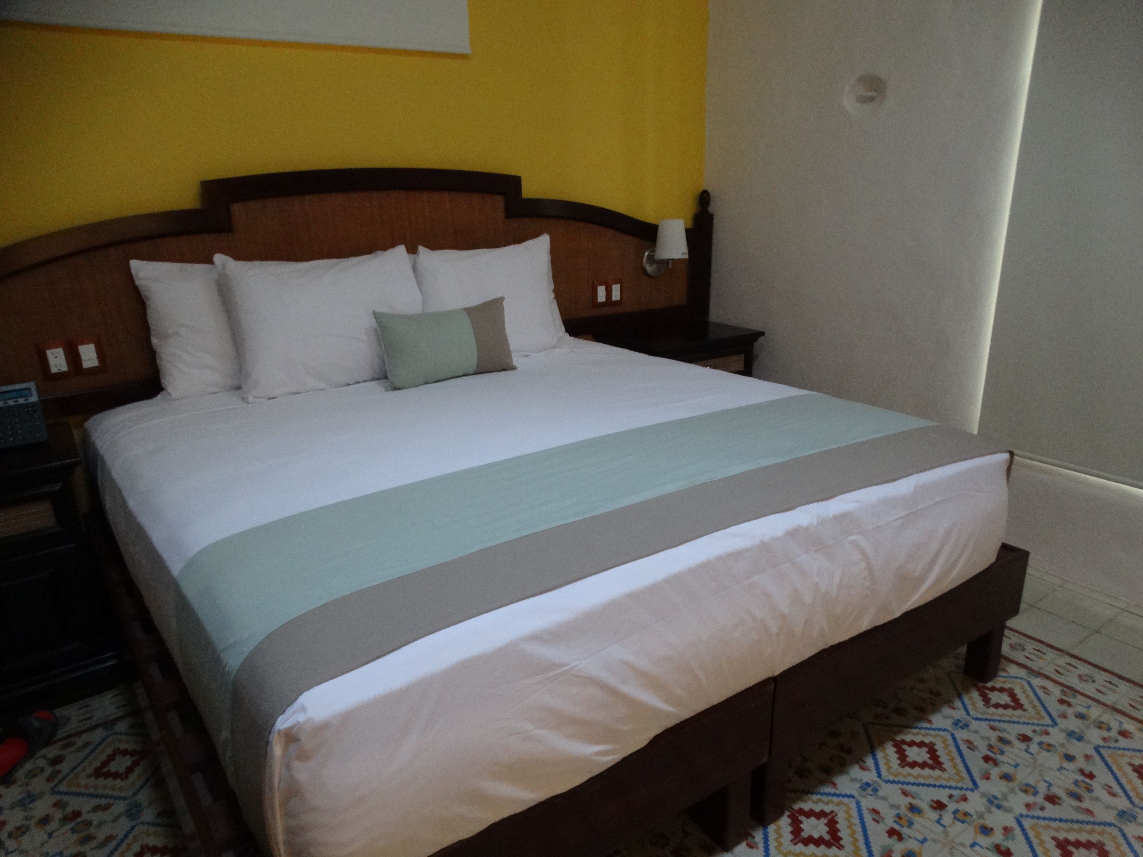 Una cama bien hecha con cabecera de madera, ropa de cama blanca y una manta clara.