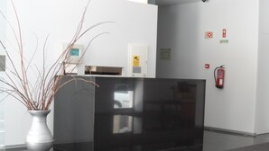 A reception area with a modern black reception desk, a white vase with branches, and a fire extinguisher mounted on the wall. - Lazza Hotel (Figueira da Foz)