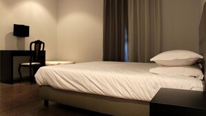 A neatly arranged bedroom with a bed, a chair, a small table, and a wall-mounted TV. - Lazza Hotel (Figueira da Foz)