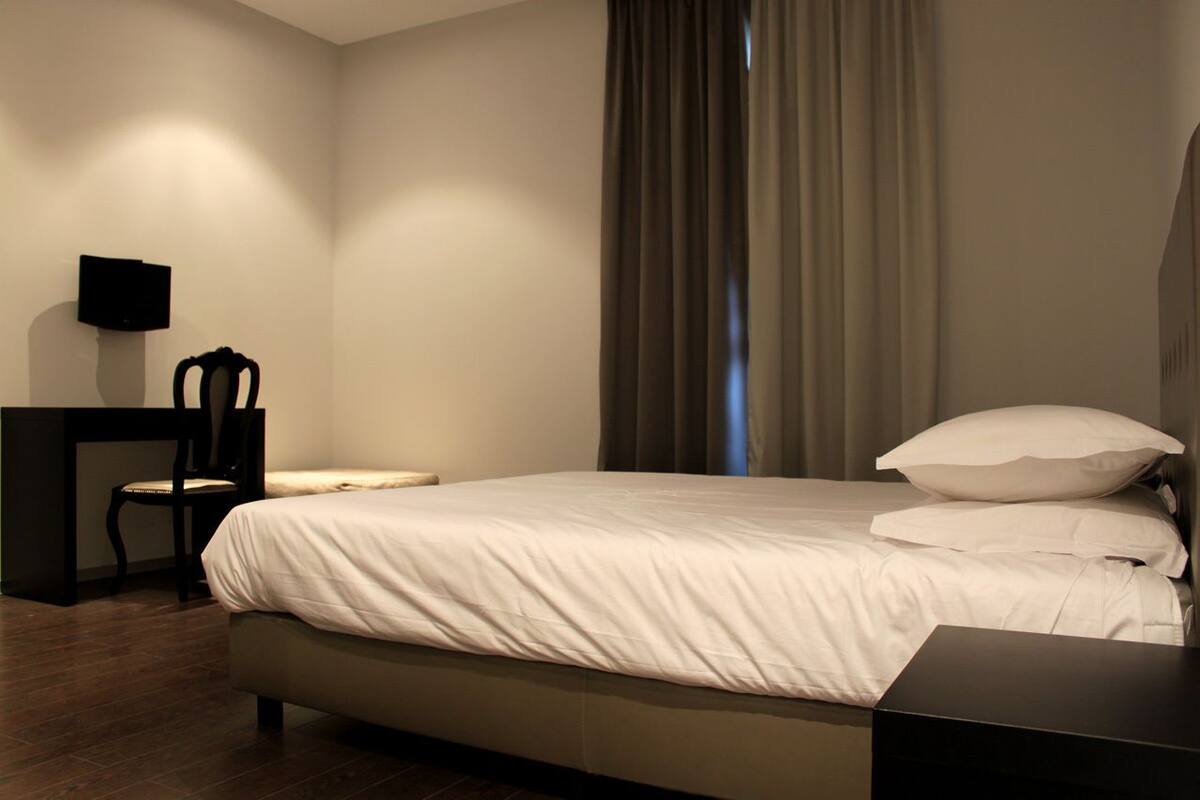 A neatly arranged bedroom with a bed, a chair, a small table, and a wall-mounted TV.
