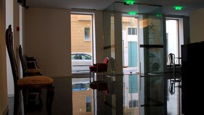 A lobby with a glass partition, chairs, and a reflection of a car outside. - Lazza Hotel (Figueira da Foz)