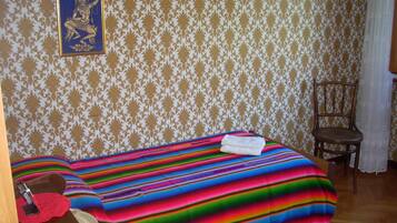 Una stanza con carta da parati decorata, un letto con coperta a righe colorate, una sedia e un quadro appeso al muro.
