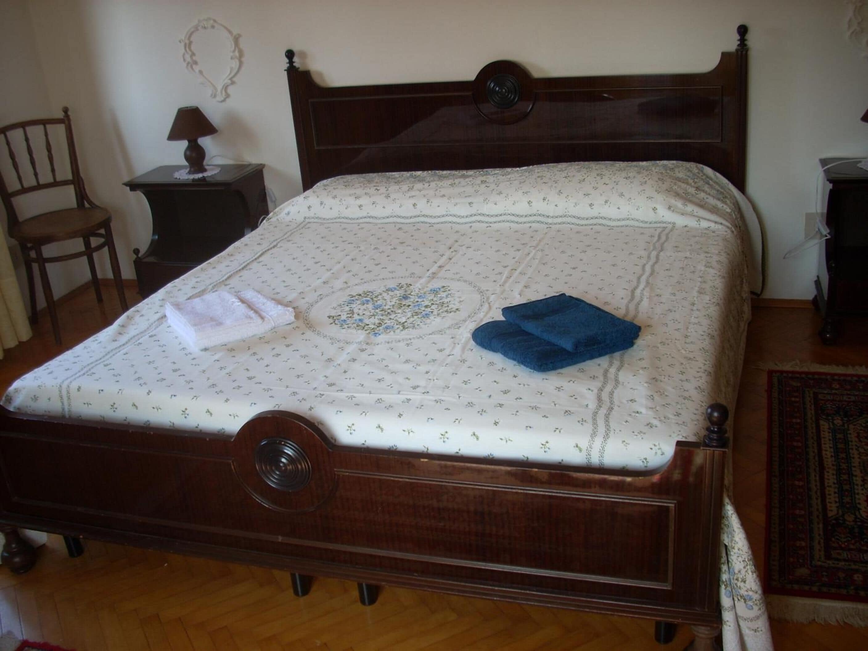 A wooden bed with a floral bedspread, a white towel, and a blue towel on it.