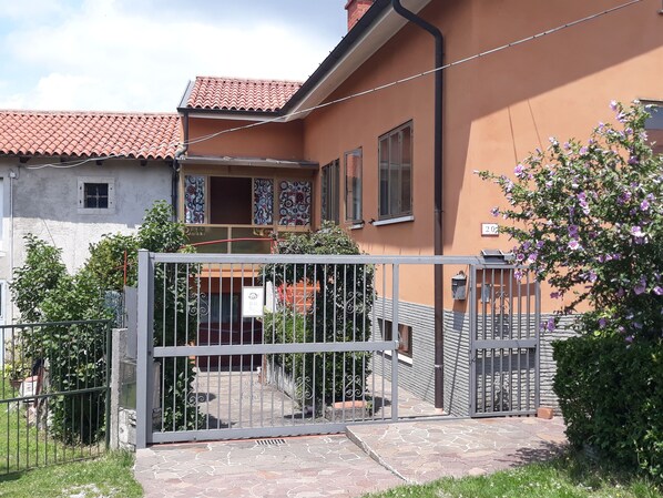 A residential building with a tiled roof, a balcony with patterned curtains, and a gated entrance.
