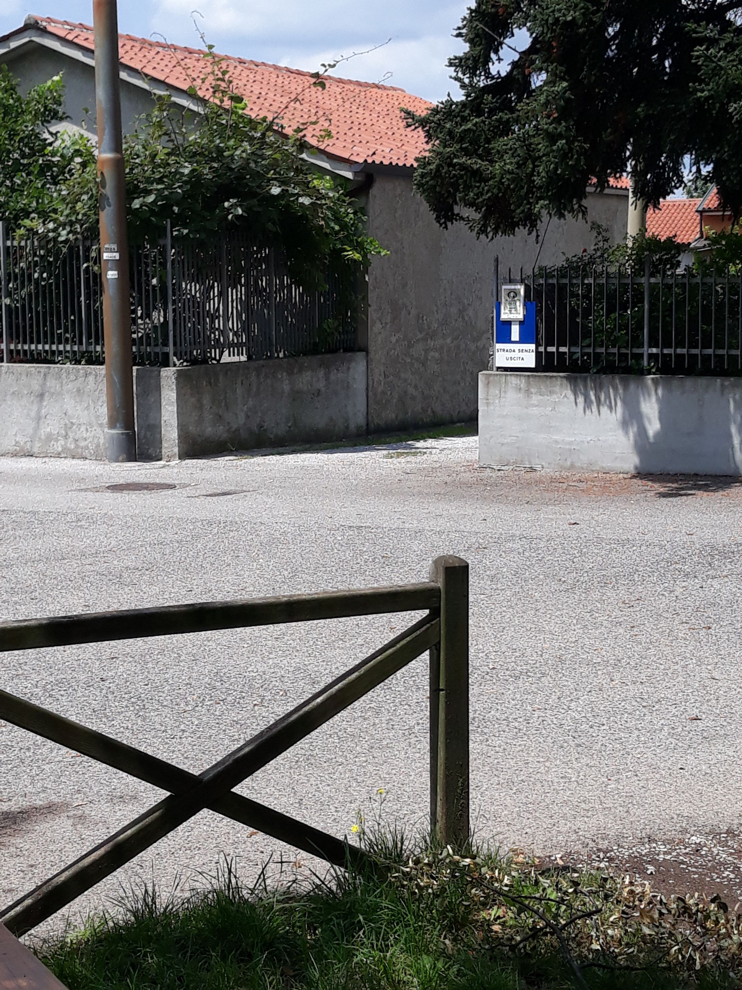 Un espace clos délimité par une clôture en métal, un mur en béton et un bâtiment surmonté d’un toit recouvert de tuiles rouges.