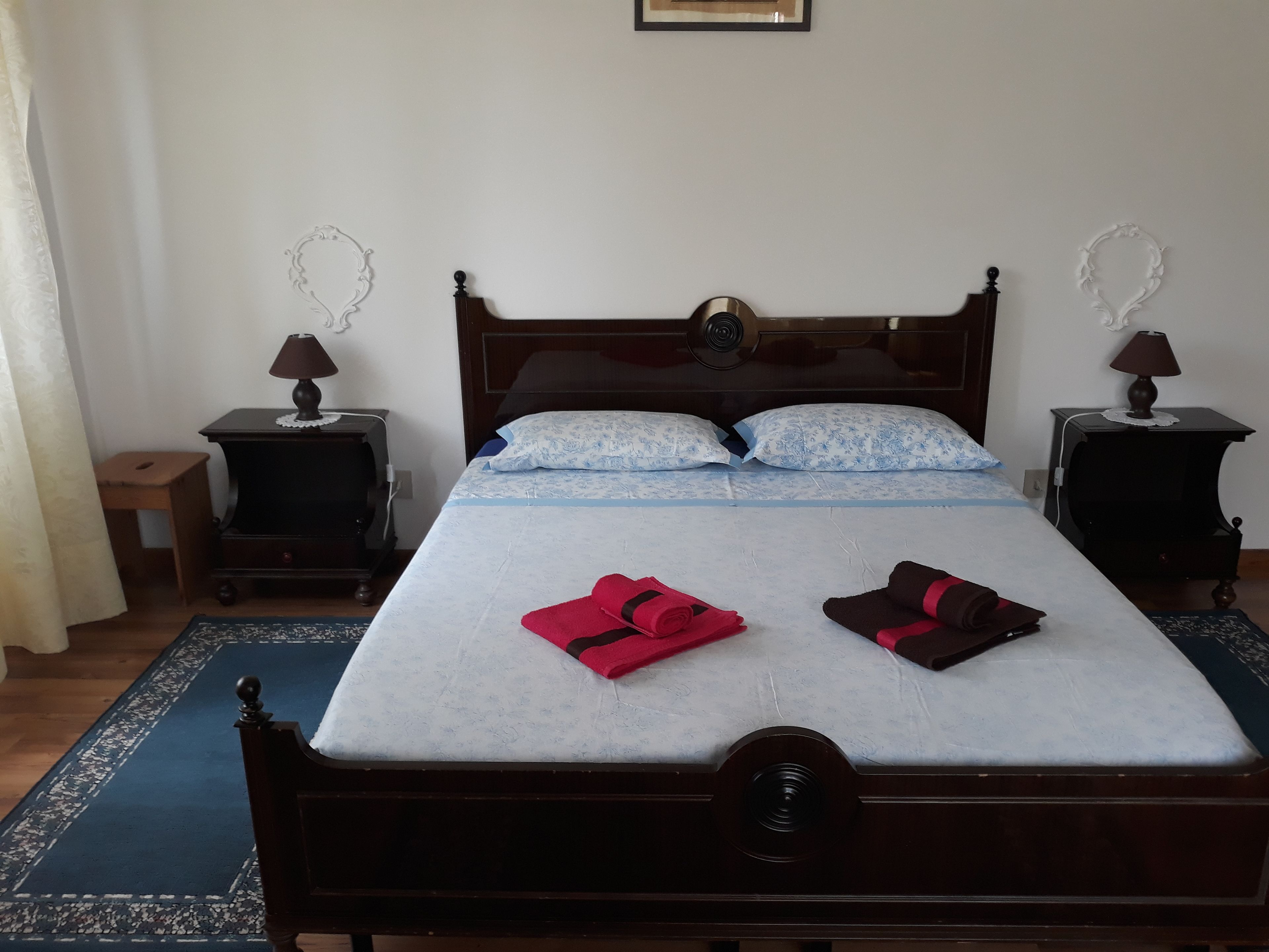A neatly made bed with a wooden headboard, two bedside tables with lamps, and a blue patterned rug.