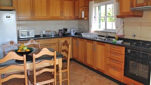 A kitchen with wooden cabinets, a black countertop, a refrigerator, a microwave, a sink, and a stove. - Casa Vista Bela by Our Madeira (Calheta)