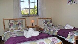 A room with two wooden beds, each with a patterned bedspread and pillows, a small bedside table with a lamp, and a window with curtains. - Casa Vista Bela by Our Madeira (Calheta)