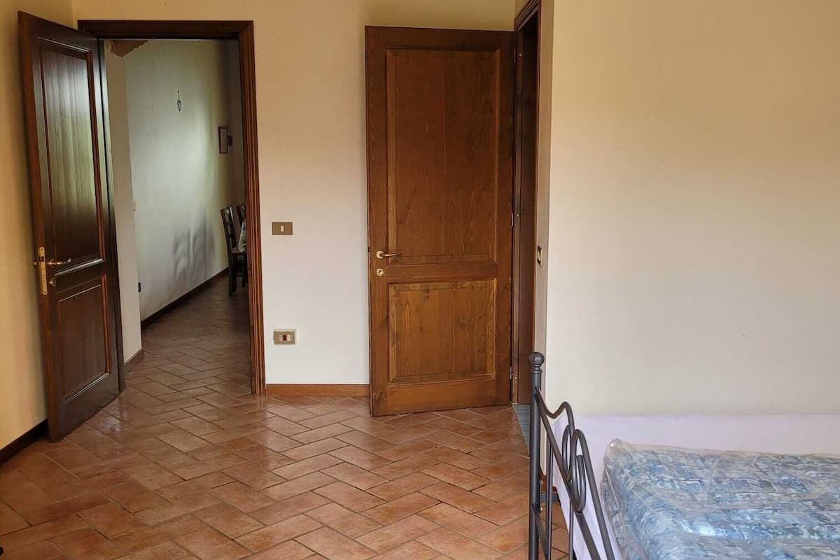 Una habitación con piso de baldosas, una cama con colchón, una puerta de madera y una lámpara.