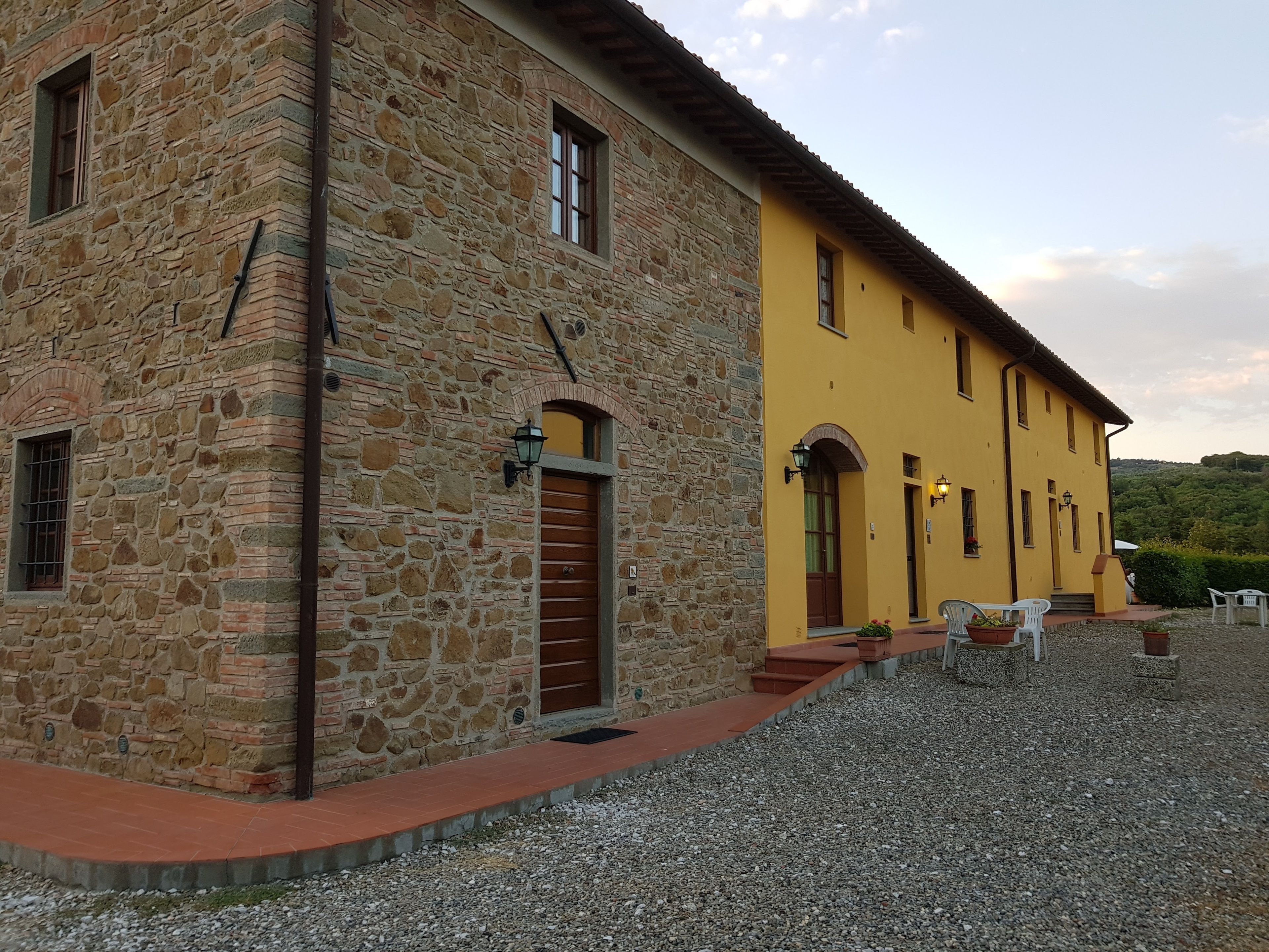 Un bâtiment en pierre et de couleur jaune, avec une allée gravillonnée et des places assises à l’extérieur.