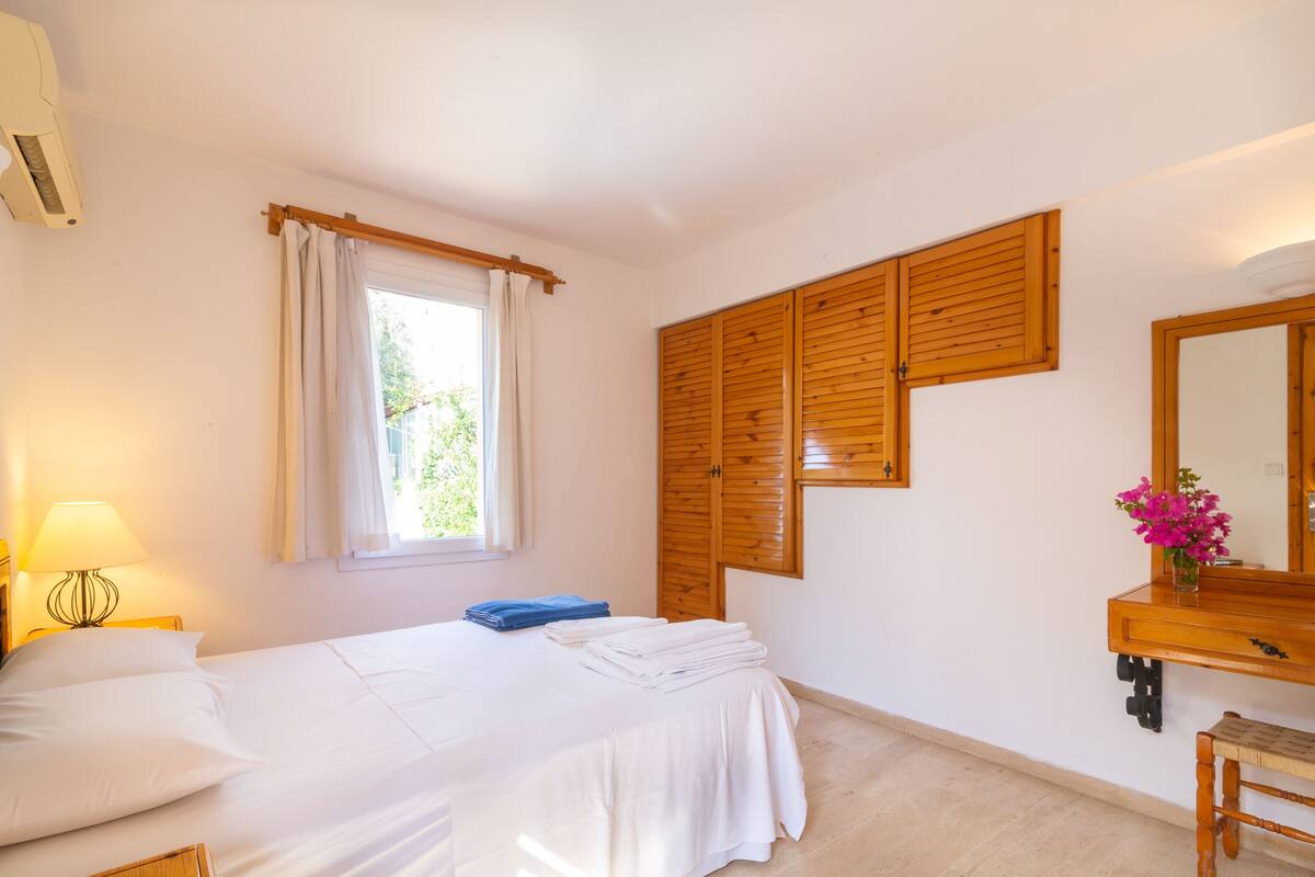 A bedroom with a bed, a wooden wardrobe, a mirror, and a window with curtains.
