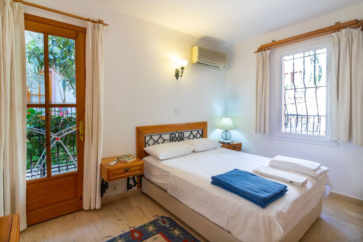 A bedroom with a bed, a nightstand, a lamp, and a window with curtains.