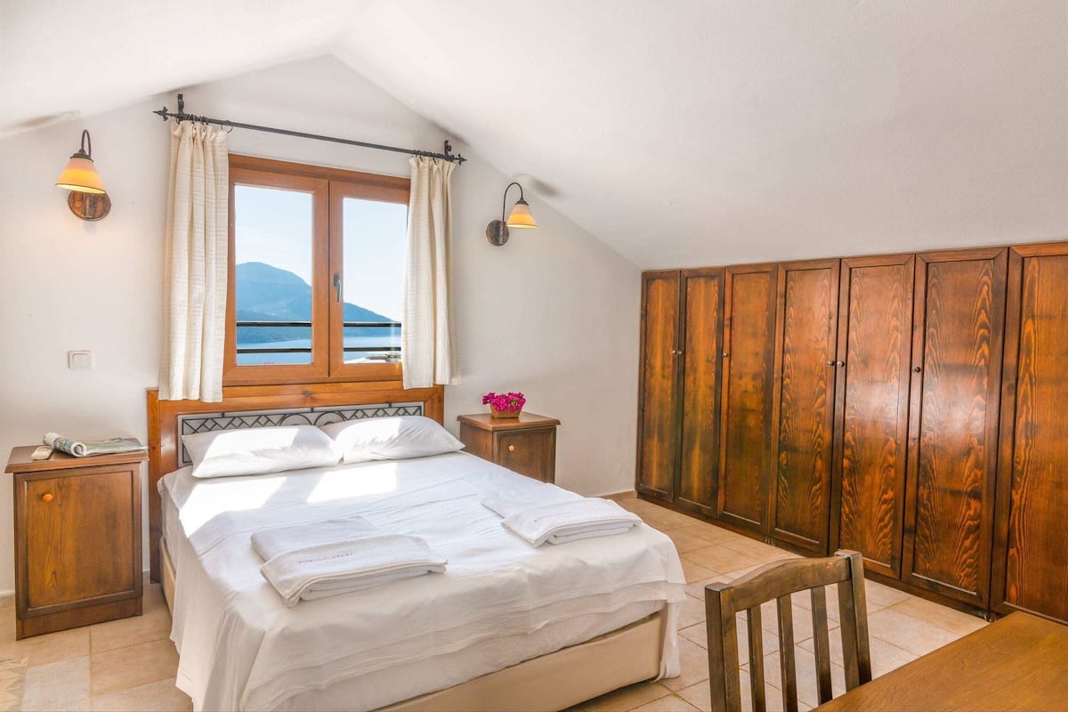 A bedroom with a bed, wooden wardrobe, and a window with curtains.