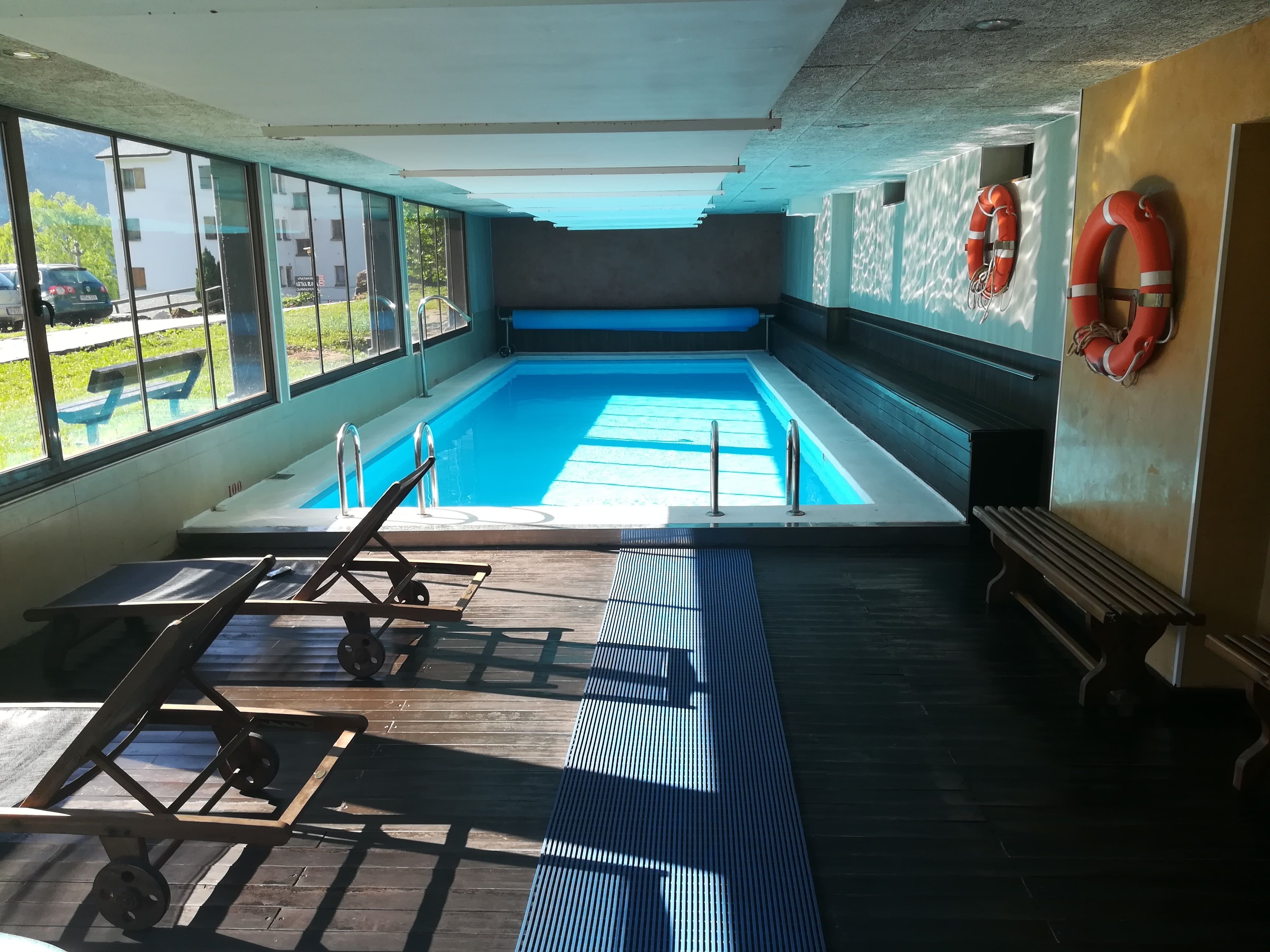 An indoor swimming pool with a view of the outside, a lifebuoy on the wall, and a bench.