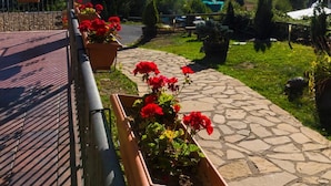 Un sendero de piedra con flores rojas, una farola y montañas al fondo.