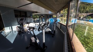 Un gimnasio con bicicletas estáticas y cinta de correr, ventanas amplias y vistas a un paisaje verde.