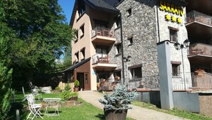 Un hotel con fachada de piedra, varios balcones y mobiliario exterior.