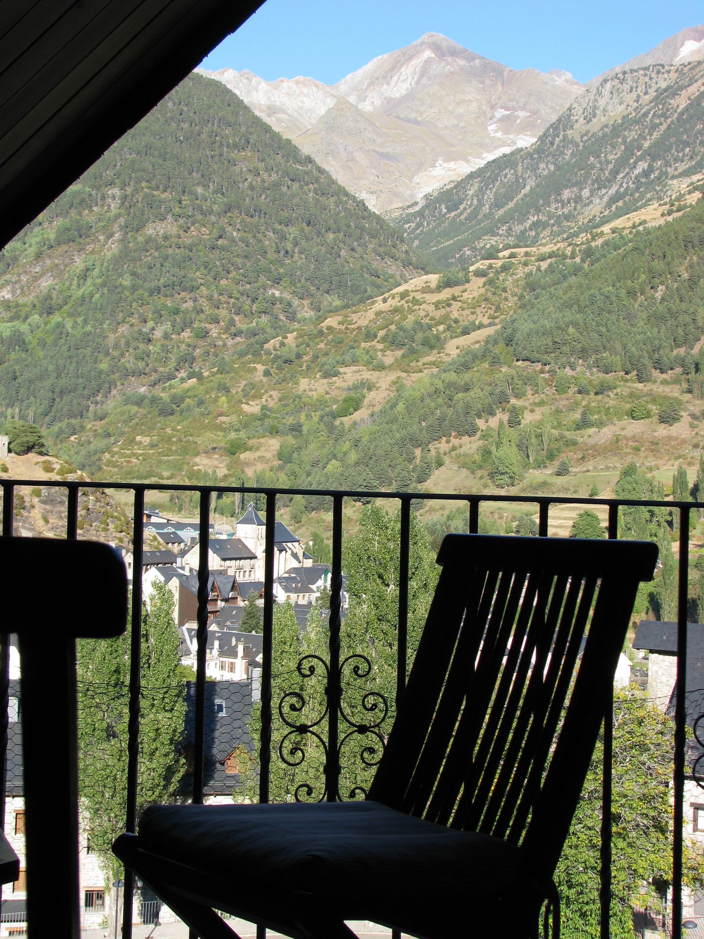 Een balkon met uitzicht op een bergachtig landschap, een stoel en een gebouw met traditionele architectuur.