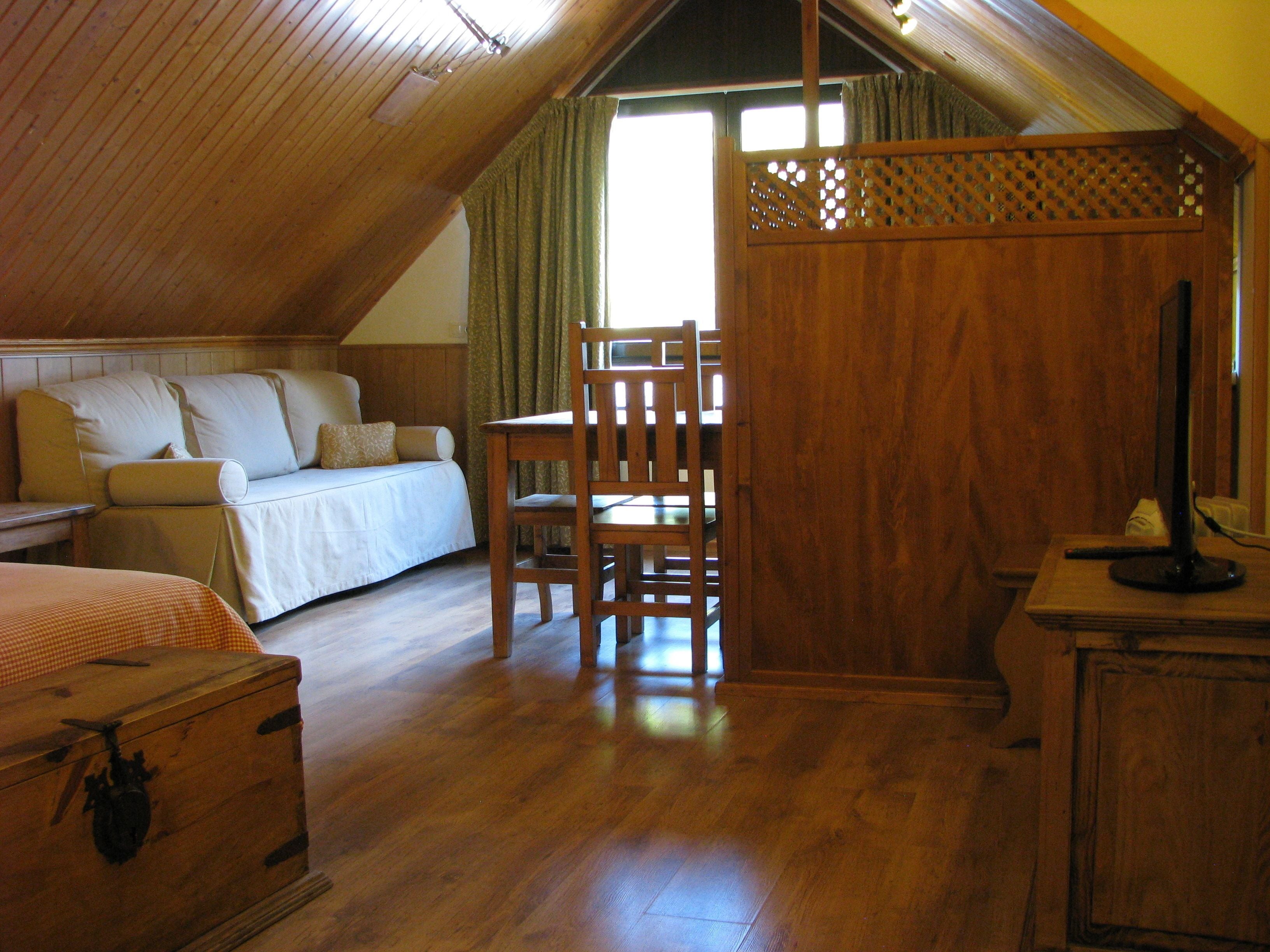 Un dormitorio acogedor en un ático con techo de madera, una cama, un escritorio de madera y una silla.