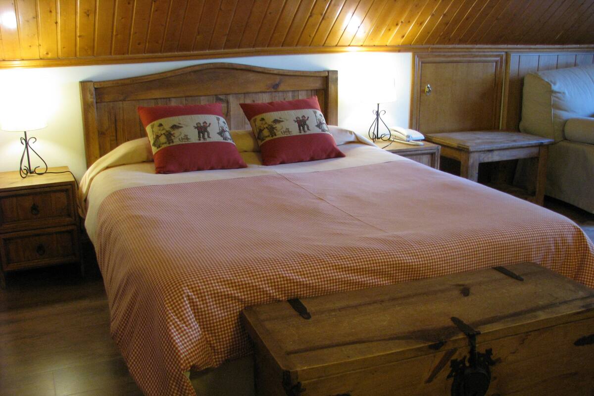 A wooden-paneled room with a bed, two bedside tables, a nightstand, and a wooden chest.