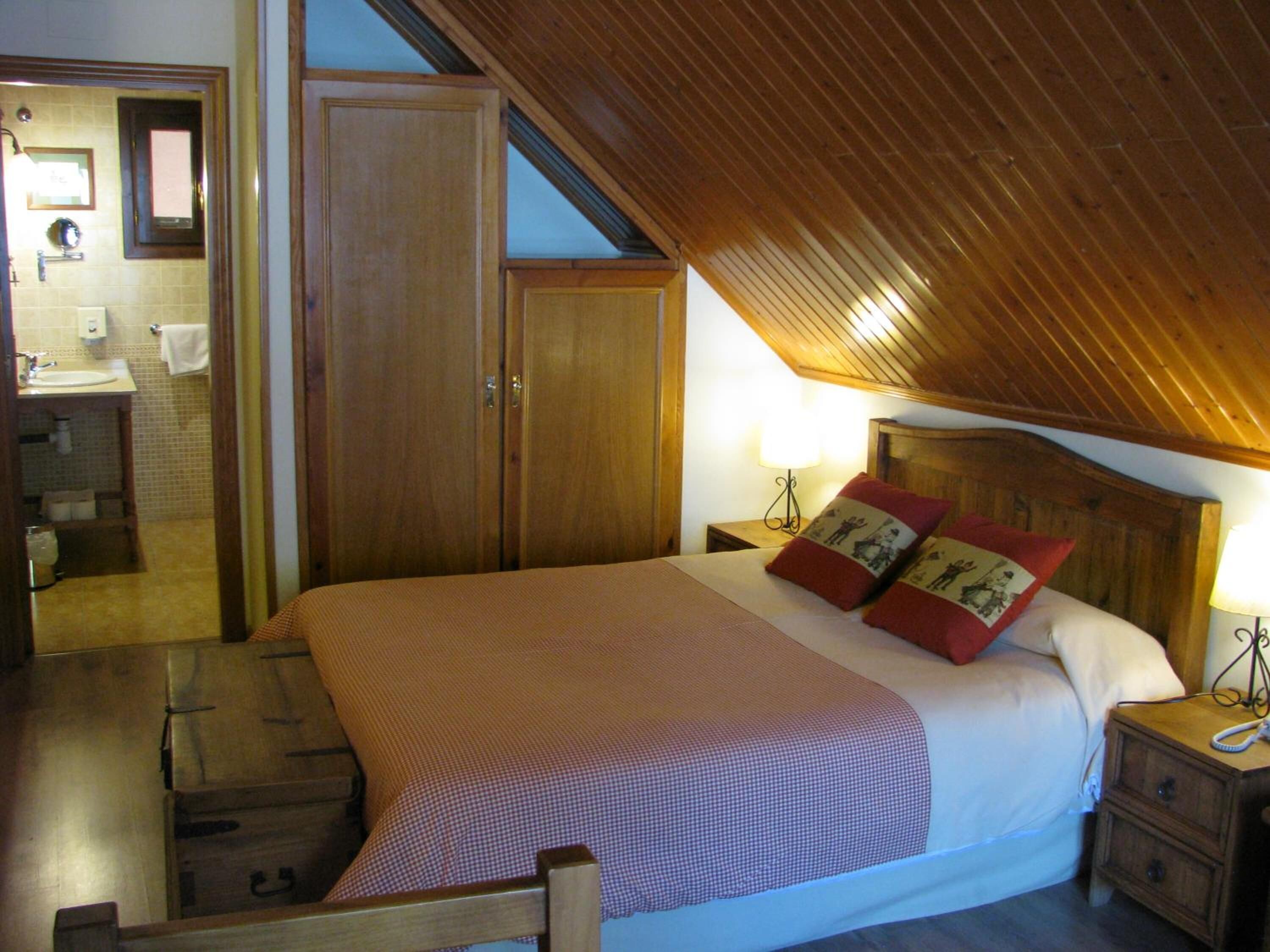 Un dormitorio con techo de madera, una cama grande con dos almohadas, una mesita de noche y un armario de madera.