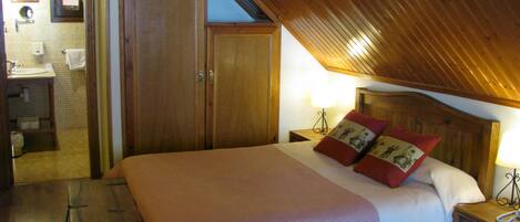 Un dormitorio con techo de madera, una cama grande con dos almohadas, una mesita de noche y un armario de madera.