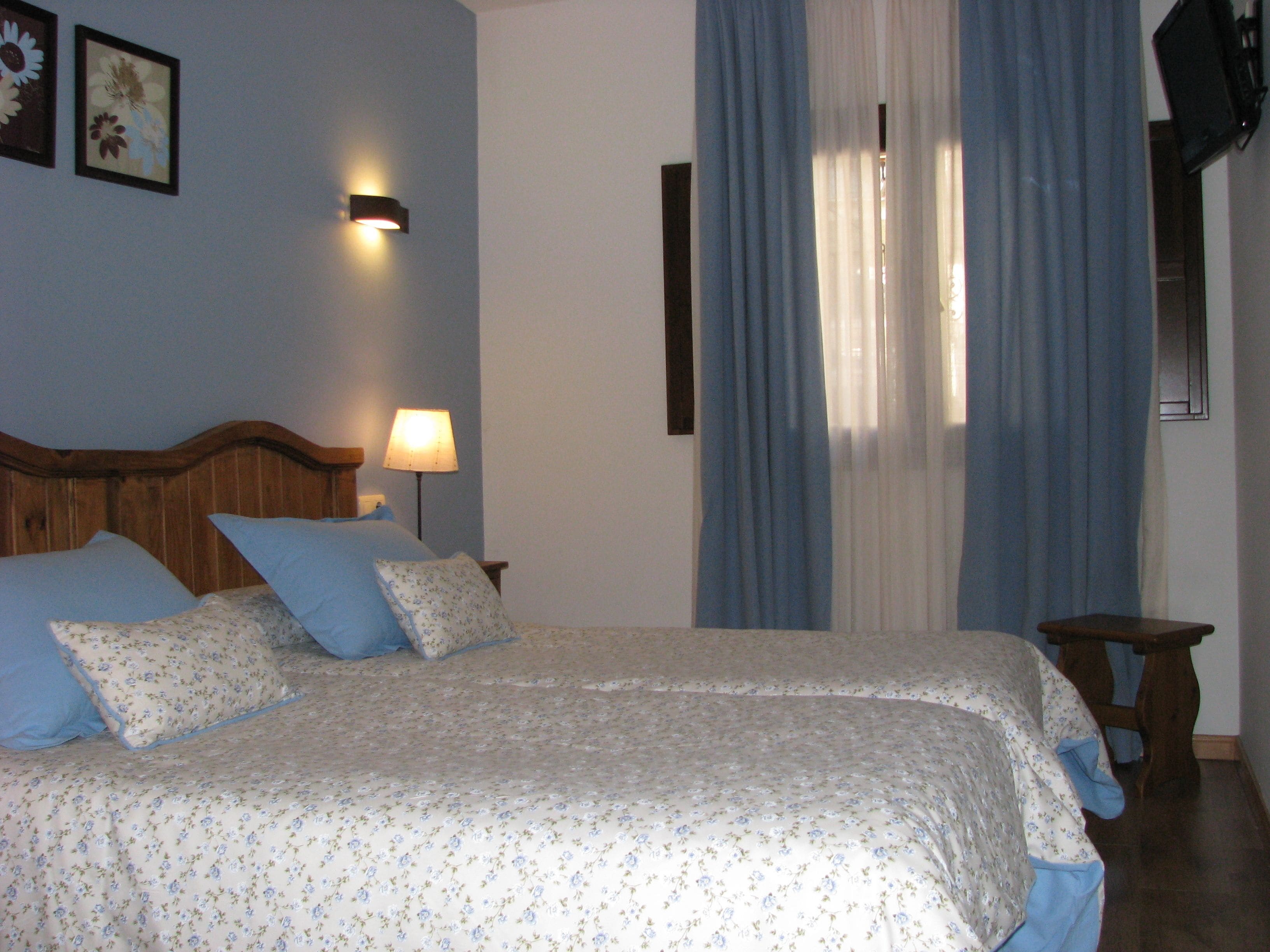 Ein Schlafzimmer mit hölzernem Kopfteil, floralem Bettbezug, einer Nachttischlampe und einem kleinen Holzschemel.