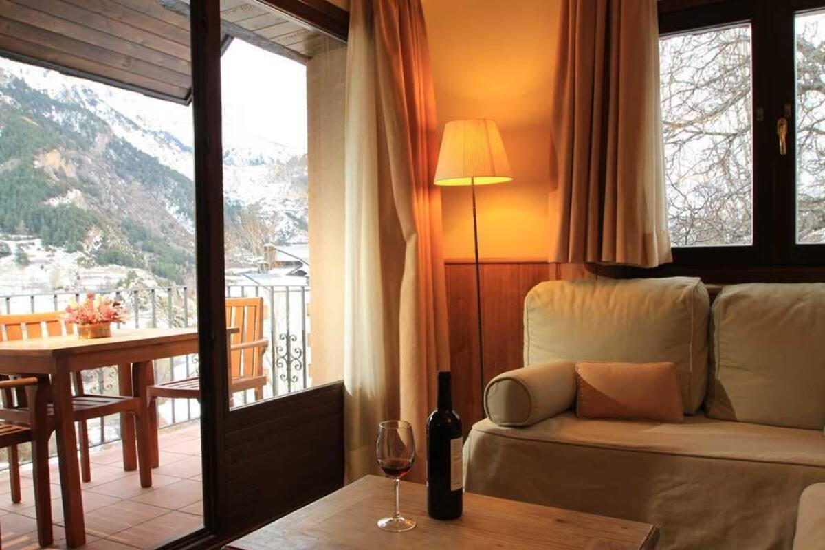 A cozy room with a wooden table, a sofa, and a view of snow-covered mountains.