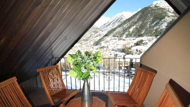 Un balcón con sillas y mesa de madera, con vistas a un paisaje montañoso.