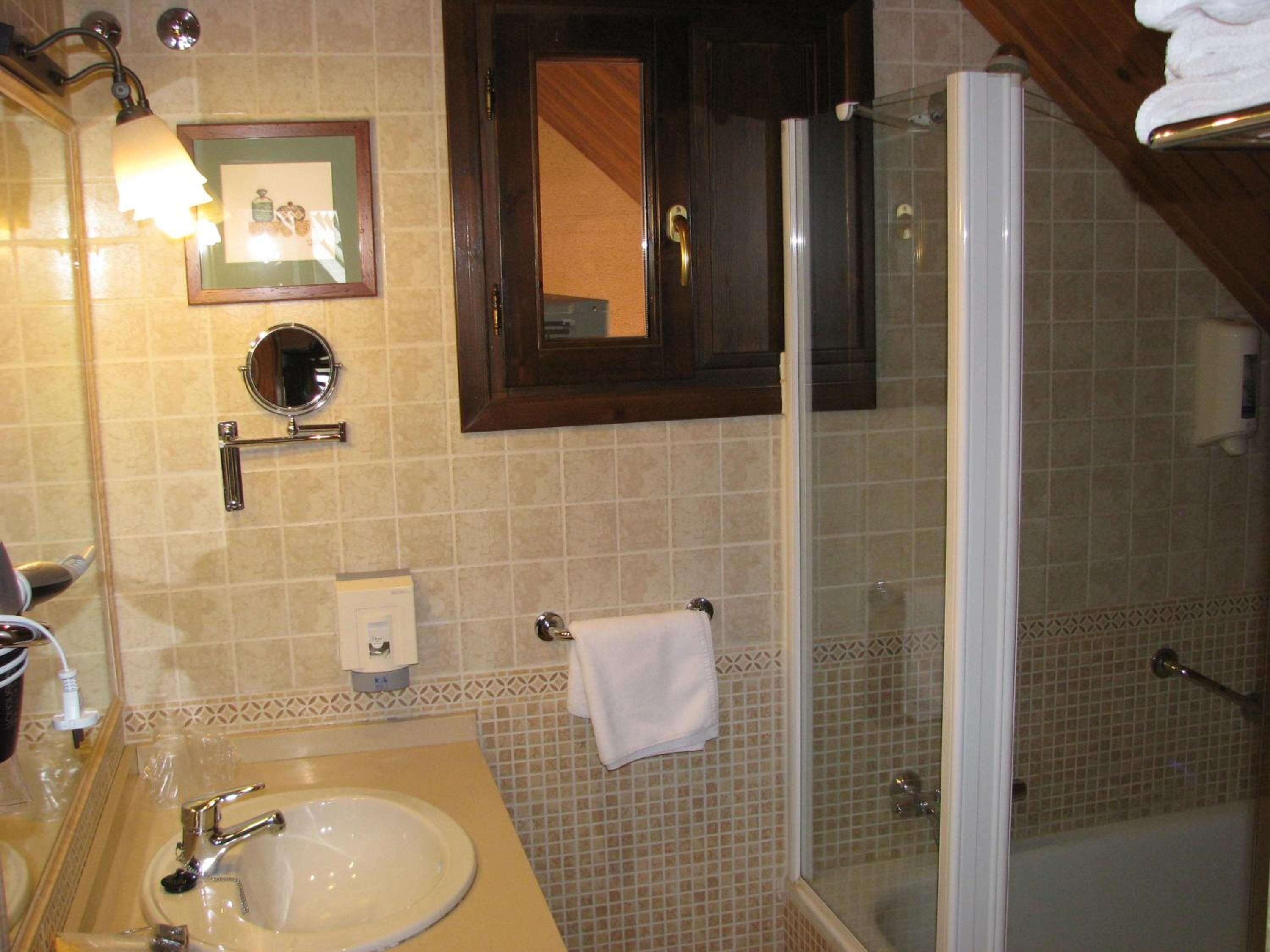 Un baño con lavamanos, espejo, toallero y cabina de ducha de vidrio.