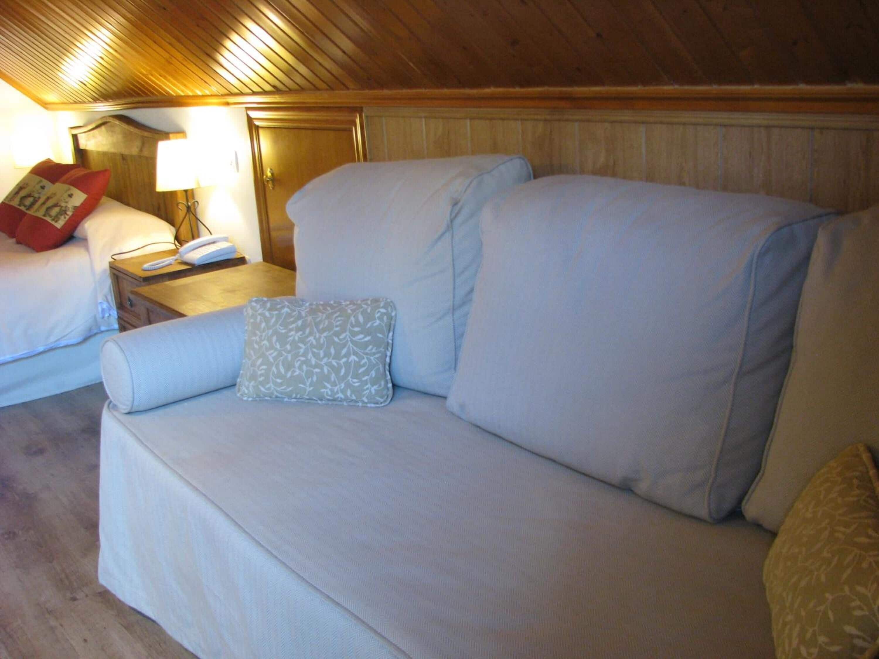 A cozy room with a large bed, a bedside table with a lamp, and a sofa with pillows.