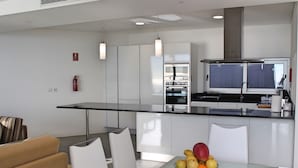 Una cocina moderna con armarios blancos, una mesa de comedor de cristal y un frutero.