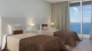 Habitación de hotel con dos camas, un ventanal con vista al mar y un balcón.