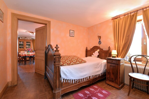A bedroom with a wooden bed, a nightstand, a chair, and a view of a dining area.