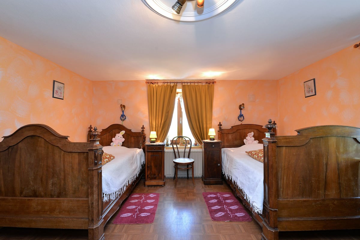 Une pièce avec deux lits en bois, une chaise, un radiateur et une fenêtre avec des rideaux.