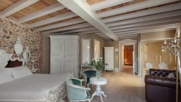 Une pièce spacieuse avec un grand lit, un mur en pierre et un plafond en bois. On y trouve des armoires blanches, une table ronde avec un vase et un canapé en cuir marron.