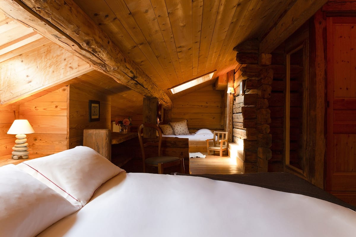 A cozy log cabin bedroom with a bed, a desk, a chair, and a stone wall.