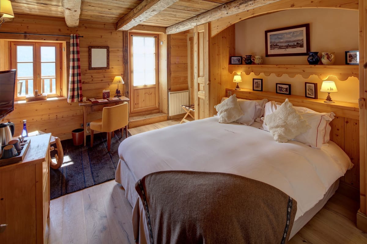A cozy wooden room with a large bed, a desk, and a chair.